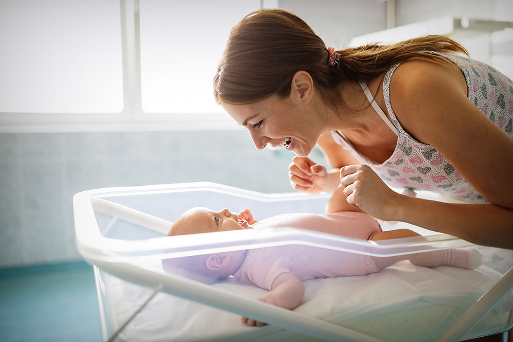 Loving mom playing first games with her baby in bedroom